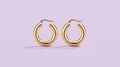 Chunky gold hoop earrings on a lilac background