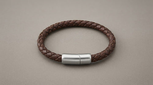 Braided brown leather bracelet with steel clasp on a warm grey background