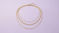 Three layered gold chain necklaces on a lavender background