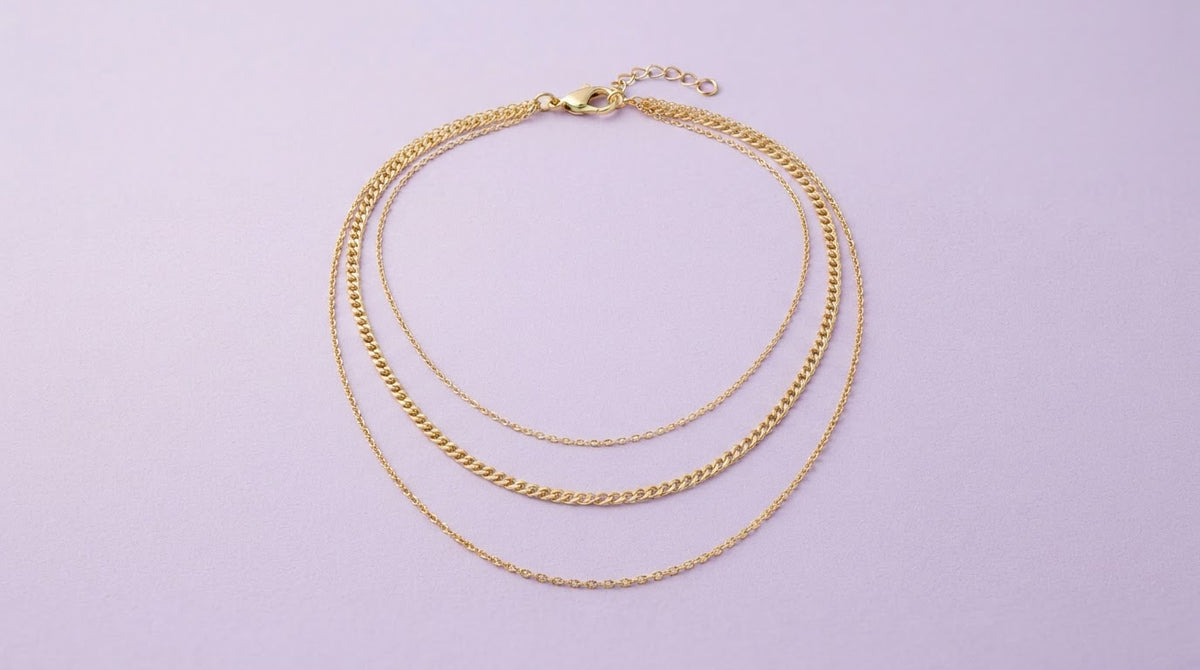 Three layered gold chain necklaces on a lavender background