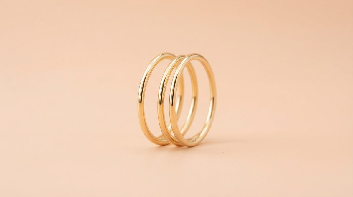 Three thin gold stacking rings on a peach background