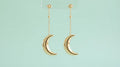 Gold crescent moon drop earrings on a mint background