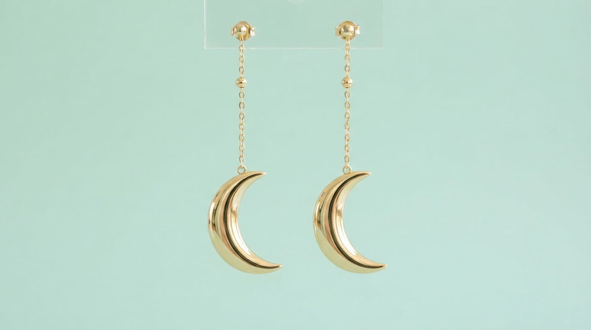 Gold crescent moon drop earrings on a mint background