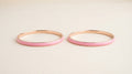 Two slim pink enamel bangles on a cream background