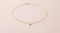 Fine gold chain necklace with a star pendant on a pale pink background