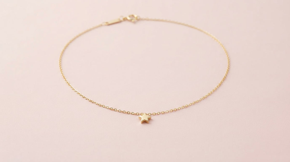 Fine gold chain necklace with a star pendant on a pale pink background